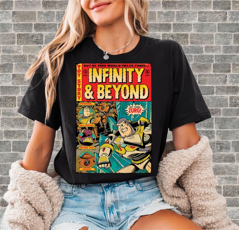 Puede incluir: Camiseta negra con un dise&ntilde;o de c&oacute;mic. El gr&aacute;fico presenta las palabras "INFINITY & BEYOND" en amarillo y rojo, e im&aacute;genes de personajes de Toy Story. El texto "ZURG!" est&aacute; en un bocadillo.