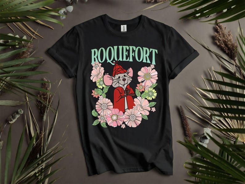Peut inclure: T-shirt noir avec le mot "ROQUEFORT" en vert menthe au-dessus d'une souris de dessin anim&eacute; portant une cape et un chapeau rouges, entour&eacute;e de fleurs roses, vertes et blanches. Le t-shirt a un col rond.