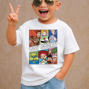 May include: White t-shirt featuring a colorful graphic of characters from the animated film "Toy Story." The design includes Woody, Buzz Lightyear, and other characters, with the words "TOY STORY" in bold letters.