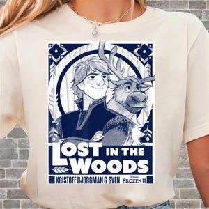 Puede incluir: Camiseta color crema con un gr&aacute;fico azul y blanco de la pel&iacute;cula Frozen II. El gr&aacute;fico incluye el texto "LOST IN THE WOODS" e im&aacute;genes de Kristoff, Sven el reno y el logotipo de Disney. Es una prenda de vestir informal.