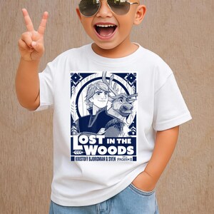 Puede incluir: Camiseta blanca con un gr&aacute;fico azul de Kristoff y Sven de Frozen II, con el texto "LOST IN THE WOODS". La camiseta es de cuello redondo y la lleva un ni&ntilde;o.