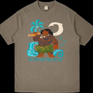 Puede incluir: Camiseta verde oliva descolorida con una ilustraci&oacute;n de dibujos animados de una figura polinesia. La figura tiene tatuajes, una falda de hierba y un arma. El dise&ntilde;o incluye una palmera, olas y una luna creciente.