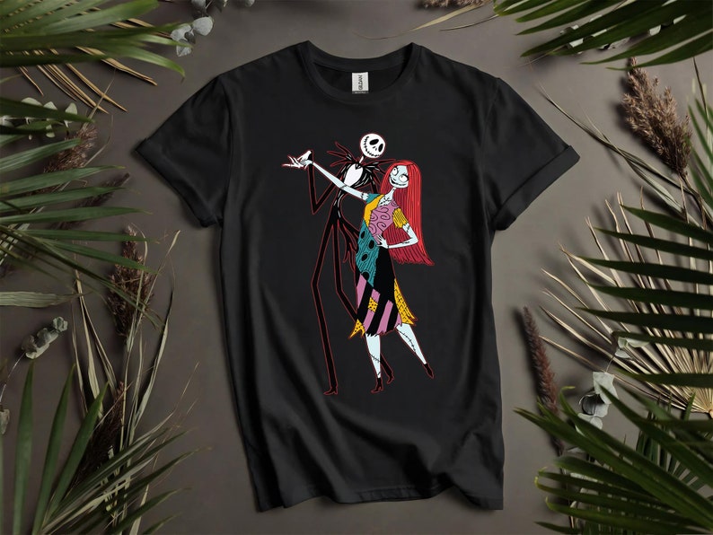 May include: Black t-shirt with a graphic of Jack Skellington and Sally from The Nightmare Before Christmas. Jack is in a black suit with red accents, and Sally is in a patchwork dress with red hair. The design is centered on the shirt.