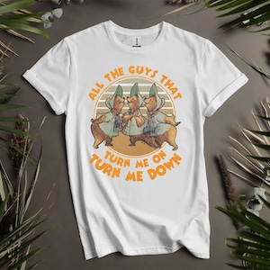 Puede incluir: Camiseta blanca con un gráfico retro de tres osos de dibujos animados con sombreros y el texto "All the guys that turn me on turn me down."