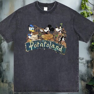 May include: Dark gray t-shirt featuring a graphic of Donald Duck, Mickey Mouse, and Goofy on a roller coaster with the text "Potatoland". The design has a vintage, distressed look.