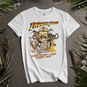 May include: White t-shirt featuring a graphic of Indiana Jones and other characters from the film. The text "Indiana Jones" and "Where there's a whip, there's a way" is printed on the shirt.