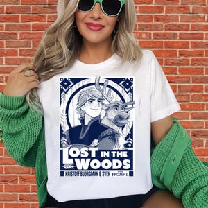 Puede incluir: Camiseta blanca con un gr&aacute;fico de Kristoff y Sven de Frozen II, con el texto "Lost in the Woods". El dise&ntilde;o utiliza tonos azules y blancos, con elementos decorativos de borde. Un producto de Disney Frozen II.