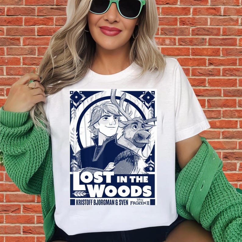 Puede incluir: Camiseta blanca con un gr&aacute;fico de Kristoff y Sven de Frozen II, con el texto "Lost in the Woods". El dise&ntilde;o utiliza tonos azules y blancos, con elementos decorativos de borde. Un producto de Disney Frozen II.