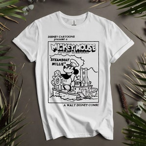 May include: White t-shirt with a black and white illustration of Mickey Mouse as a steamboat captain. The text reads "DISNEY CARTOONS present a MICKEY MOUSE SOUND CARTOON 'STEAMBOAT WILLIE' A WALT DISNEY COMIC".