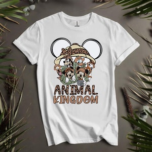 Puede incluir: Camiseta blanca con un gr&aacute;fico de Mickey Mouse y sus amigos vestidos como exploradores de safari. El gr&aacute;fico incluye un sombrero de estampado de leopardo y el texto "Animal Kingdom".