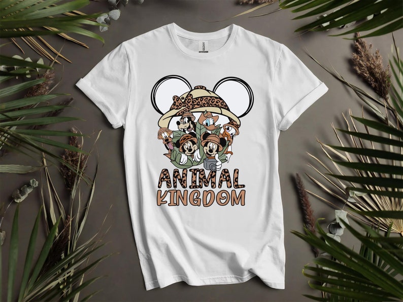 Puede incluir: Camiseta blanca con un gr&aacute;fico de Mickey Mouse y sus amigos vestidos como exploradores de safari. El gr&aacute;fico incluye un sombrero de estampado de leopardo y el texto "Animal Kingdom".