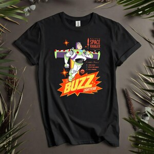 Puede incluir: Camiseta negra con un gr&aacute;fico de Buzz Lightyear de la pel&iacute;cula Toy Story. El dise&ntilde;o incluye a Buzz con su traje de guardi&aacute;n espacial, las palabras "BUZZ LIGHTYEAR" y otro texto. La camiseta est&aacute; rodeada de hojas verdes.