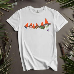 Puede incluir: Camiseta blanca con un dise&ntilde;o de dibujos animados de personajes que llevan sombreros de cono de tr&aacute;fico naranja. El dise&ntilde;o incluye a Buzz Lightyear y otras figuras en verde y marr&oacute;n. La camiseta es de material suave.