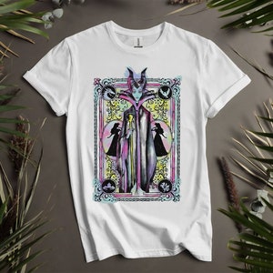 May include: White t-shirt with a colorful illustration of Maleficent from Disney's Sleeping Beauty. The illustration is framed in a decorative border with floral accents.
