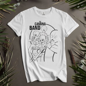 May include: White t-shirt featuring a black and white illustration of an alien band playing instruments. The text "The Cantina Band" is printed on the shirt.