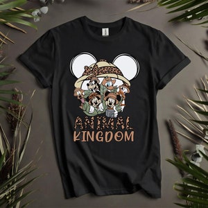 Puede incluir: Camiseta negra con un gr&aacute;fico de Mickey Mouse y sus amigos vestidos como exploradores de safari. El gr&aacute;fico incluye un sombrero de estampado de leopardo y el texto "Animal Kingdom".
