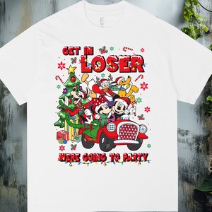 Puede incluir: Camiseta blanca con un diseño festivo de Mickey Mouse, Minnie Mouse, Donald y Pluto en un coche rojo. El texto "GET IN LOSER WE'RE GOING TO PARTY" se muestra encima y debajo de los personajes, con detalles navideños.