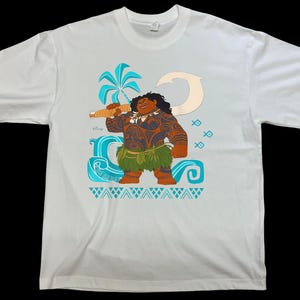 Puede incluir: Camiseta blanca con una ilustraci&oacute;n de dibujos animados de un personaje polinesio sosteniendo un arma. El personaje tiene piel morena, tatuajes y una falda de hierba. El dise&ntilde;o incluye una palmera, olas y peces en tonos azules y turquesas.