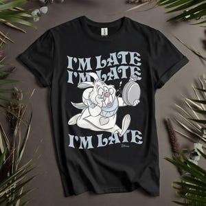 May include: Black t-shirt featuring the White Rabbit from Alice in Wonderland, running and holding a pocket watch. The text "I'M LATE" is printed in light blue above and below the rabbit. The Disney logo is at the bottom.