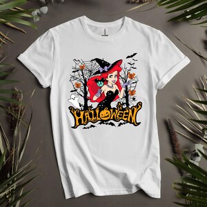 Puede incluir: Camiseta blanca con un gr&aacute;fico de una mujer pelirroja con un sombrero de bruja y sosteniendo una calabaza de Mickey Mouse. El gr&aacute;fico tambi&eacute;n incluye murci&eacute;lagos, fantasmas y la palabra "HALLOWEEN".