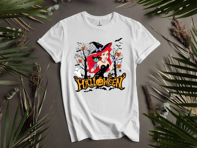 Puede incluir: Camiseta blanca con un gr&aacute;fico de una mujer pelirroja con un sombrero de bruja y sosteniendo una calabaza de Mickey Mouse. El gr&aacute;fico tambi&eacute;n incluye murci&eacute;lagos, fantasmas y la palabra "HALLOWEEN".