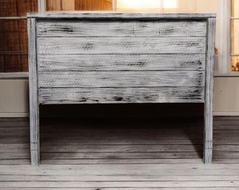 Puede incluir: Cabecero de madera blanqueada con un acabado rústico y desgastado. El cabecero tiene un diseño simple y rectangular con una parte superior plana y lados rectos.