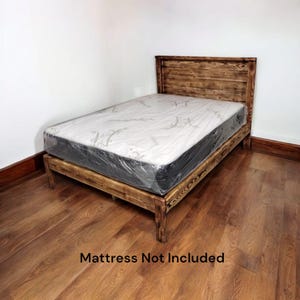 Puede incluir: Un marco de cama de madera r&uacute;stico con una cabecera de listones. El marco de la cama est&aacute; hecho de madera recuperada y tiene un acabado natural. El colch&oacute;n no est&aacute; incluido. "Mattress Not Included" est&aacute; escrito en negro en el suelo.