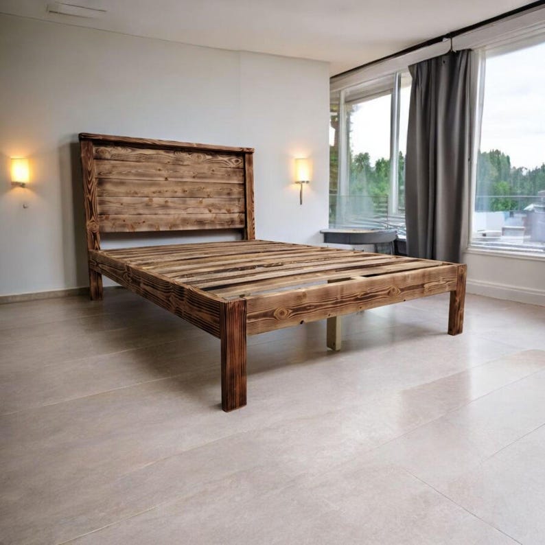 Puede incluir: Un marco de cama de madera r&uacute;stica con una cabecera hecha de tablones de madera recuperados. El marco tiene una base de listones y est&aacute; te&ntilde;ido de un color marr&oacute;n oscuro.