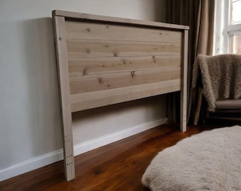 Puede incluir: Un cabecero de madera clara con un marco rectangular y tablones horizontales. El cabecero está hecho de madera natural y se apoya contra una pared blanca. El cabecero es de estilo rústico y es un mueble de dormitorio.