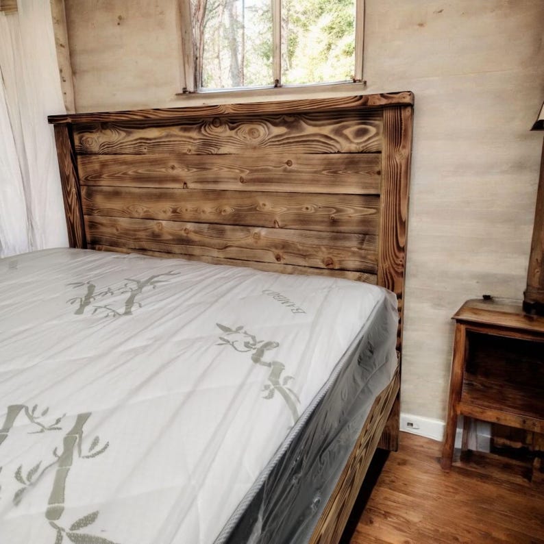 Puede incluir: Una cabecera de cama de madera r&uacute;stica con un acabado de madera natural. La cabecera est&aacute; hecha de madera recuperada y tiene un aspecto desgastado. La cabecera est&aacute; unida a un marco de cama con un colch&oacute;n blanco.