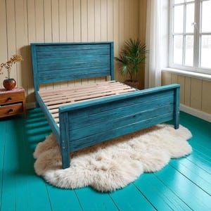 May include: A teal-painted wooden bed frame with a slatted headboard and footboard. The bed sits on a fluffy, cream-colored rug. The room has teal-painted floors and a neutral-toned wall. A small wooden nightstand and a potted plant are visible.