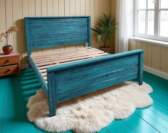 Puede incluir: Un marco de cama de madera pintado de color turquesa con cabecero y piecero de listones. La cama está sobre una alfombra esponjosa de color crema. La habitación tiene suelos pintados de color turquesa y paredes de tonos neutros. Una pequeña mesita de noche de madera y una planta en maceta son visibles.
