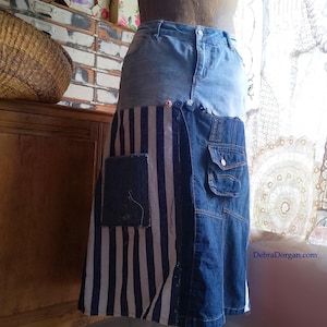 以下が含まれることがあります： 異なるデニム生地のパッチワークで作られたロングデニムスカート。スカートにはストライプのパネル、大きなポケット、小さなポケットが付いています。スカートは、さまざまな青色のデニムのパッチワークです。
