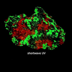 May include: A rock formation illuminated with bright green and red patches against a black backdrop. The text "shortwave UV" is visible at the bottom. The rock's surface has a mottled appearance.