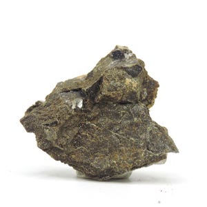 May include: A raw, irregular mineral specimen featuring a dark, earthy brown and olive green color palette. The surface is textured with jagged, uneven edges and small, embedded crystalline inclusions that catch the light, creating a rugged appearance.