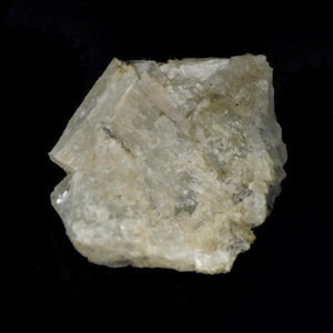 Op de afbeelding: Een close-up van een lichtgroen mineraal specimen tegen een zwarte achtergrond. Het mineraal heeft een kristallijne structuur met zichtbare lagen en een enigszins doorschijnend uiterlijk. De kleur is een zacht, gedempt groen met hints van beige.
