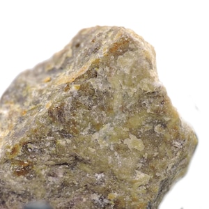 May include: Close-up of a rough, irregularly shaped rock with a mix of colors. The rock's surface displays a blend of olive green, tan, and gray hues, with a slightly crystalline texture. The lighting highlights the natural variations and mineral composition of the stone.
