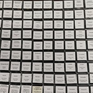 May include: A large collection of square, clear plastic display boxes arranged in a grid. Each box contains a small mineral specimen and a white label with black printed text identifying the mineral name and its specific geographic origin.