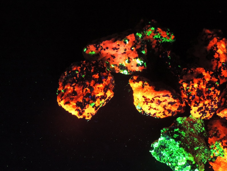 May include: Close-up of several rocks with a vibrant, glowing appearance. The rocks have a base color of orange, with patches of green and blue. The image is set against a black background, highlighting the colorful minerals.