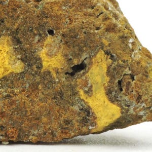 May include: A rough, textured mineral specimen featuring a mottled surface with deep brown, earthy tones and vibrant, irregular patches of bright yellow. The rock displays a porous, uneven structure with small cavities and granular mineral deposits.