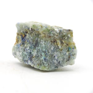 May include: A rough-hewn mineral specimen with a mix of blue, green, and brown hues. The rock has a textured surface and irregular shape, with areas of crystalline structure visible. The background is plain white.