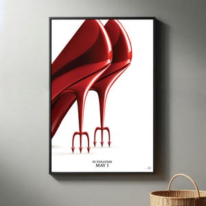 Könnte beinhalten: Gerahmtes Poster mit zwei glänzenden, roten High Heels mit dreizackförmigen Absätzen. Das Poster hat einen weißen Hintergrund und den Text "IN THEATERS MAY 1" unten. Das Bild ist vor einer neutralen grauen Wand.