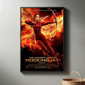 May include: A framed movie poster for "The Hunger Games: Mockingjay - Part 2." The poster features a woman in a red outfit with a bow and arrow, set against a fiery background. Text includes "Nothing Can Prepare You For The End" and "November 20."