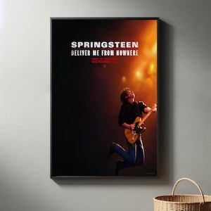 以下が含まれることがあります： 「Springsteen Deliver Me From Nowhere」の文字が入ったフレーム付きポスター。ギターを弾きながらジャンプするミュージシャンの画像。テキスト「Only in Theaters October 23」も表示されています。
