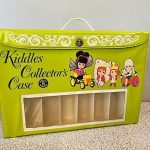 May include: A green vinyl Kiddle's Collector's Case with a clear plastic window showing six compartments. The case has a white handle and a metal latch. The front of the case features a colorful illustration of five Kiddle dolls and a Kiddle car.