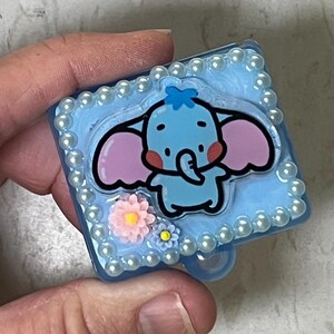 May include: A blue and white resin trinket box with a cartoon elephant design. The box is decorated with pearl-like beads around the edge and has a blue and white floral design.