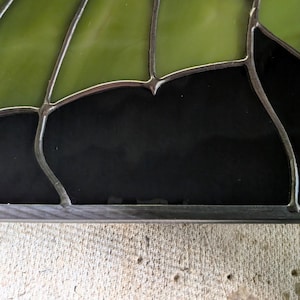 Puede incluir: Un panel de vidriera compuesto por segmentos de vidrio verde oliva transl&uacute;cido y vidrio negro opaco. Las piezas de vidrio individuales est&aacute;n unidas por l&iacute;neas de soldadura de metal oscuro, creando un patr&oacute;n geom&eacute;trico con bordes curvos.