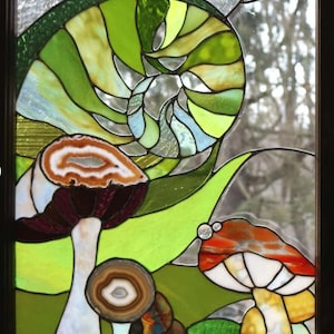 May include: Stained glass window depicting a whimsical design of mushrooms with agate slices for the caps. The mushrooms are set against a background of swirling green and blue glass.