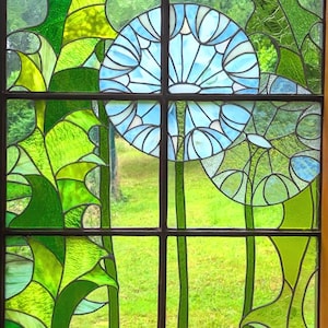 May include: A stained glass window with a blue and green floral design. The window is divided into nine panes, with a large blue flower in the center. The flower is surrounded by green leaves and stems.