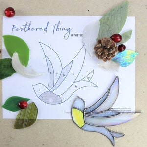 May include: A stained glass bird pattern with numbered sections, a finished stained glass bird, and various craft supplies including feathers, leaves, and pine cones.